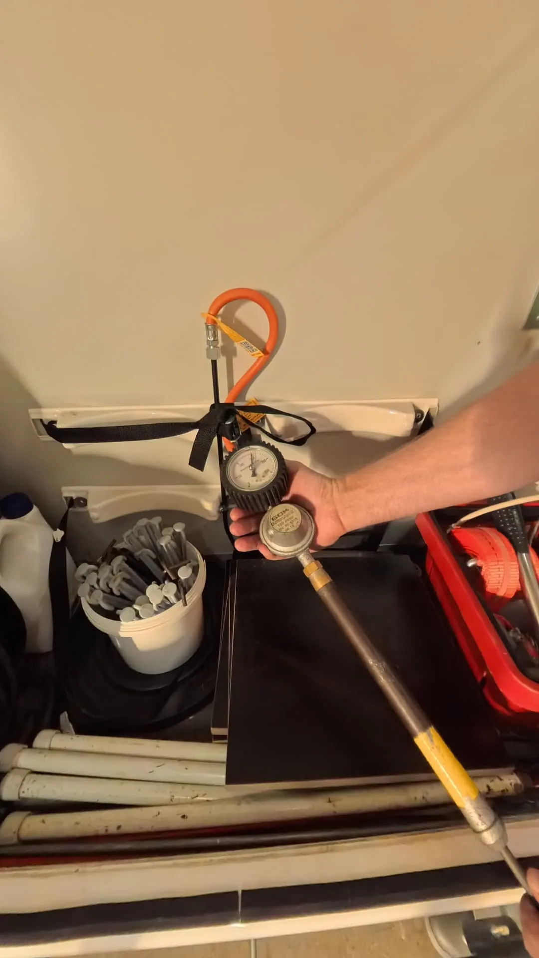 Hand mit einem Manometer und angeschlossenem Schlauch im Gasflaschenfach.